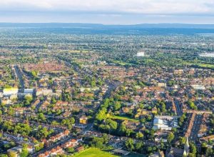Aerial photo of a city featuring grid-patterned streets, residential houses, patches of green space, and distant rolling hills.