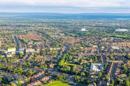 Aerial photo of a city featuring grid-patterned streets, residential houses, patches of green space, and distant rolling hills.