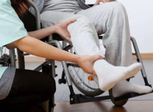 A carer assists a wheelchair user by supporting their leg, aiding in movement or therapeutic exercise.