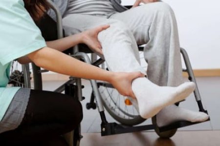 A carer assists a wheelchair user by supporting their leg, aiding in movement or therapeutic exercise.