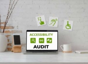 A laptop sits on a desk showing Accessibility Audit and related icons, with decor and accessibility signs visible on the wall behind.