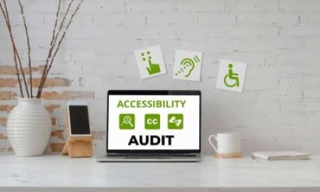 A laptop sits on a desk showing Accessibility Audit and related icons, with decor and accessibility signs visible on the wall behind.