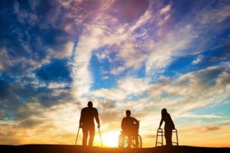 Three individuals using mobility aids—crutches, a wheelchair, and a Zimmer frame—are silhouetted against a vibrant sunset sky.