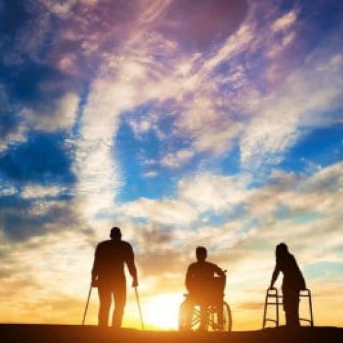 Three individuals using mobility aids—crutches, a wheelchair, and a Zimmer frame—are silhouetted against a vibrant sunset sky.
