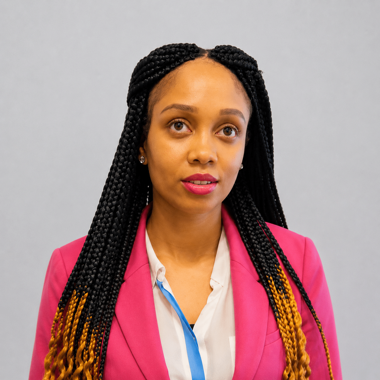 Woman with plaited hair stands against a plain grey background wearing a pink blazer over a white blouse, suitable for illustrating website accessibility or usability testing concepts.