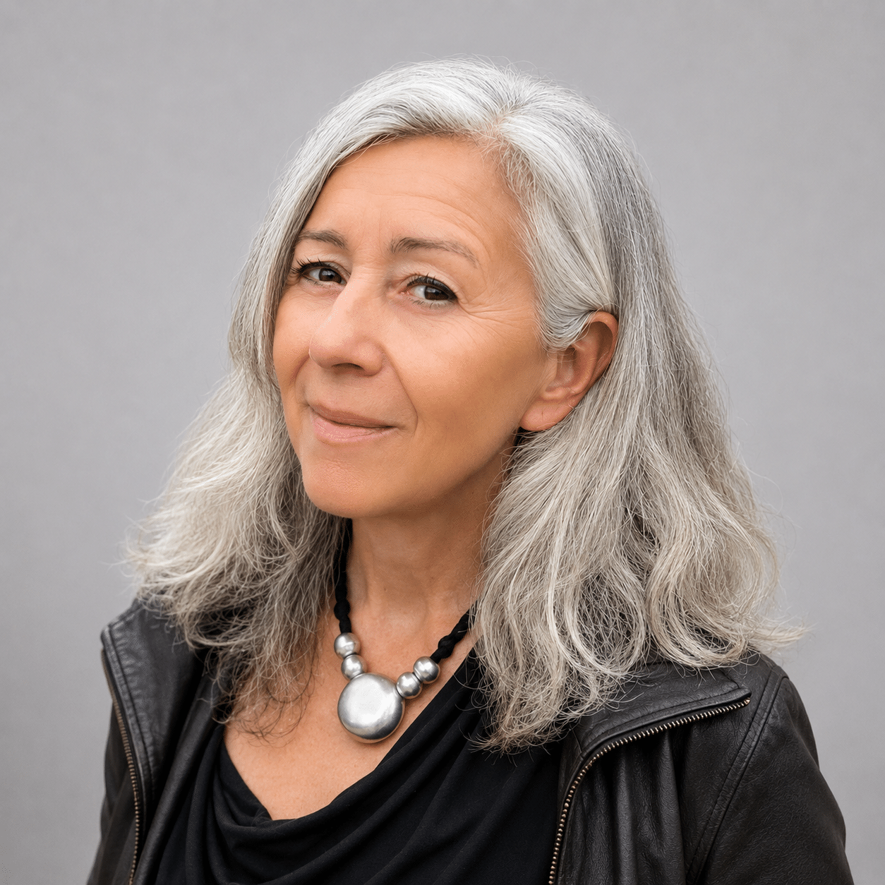 Older woman with long grey hair wearing a black top, leather jacket, and silver necklace prepares to test web features and check website accessibility.