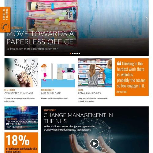 Shelves in an office are filled with piles of paper, digital devices, healthcare-related images, and signs or posters discussing paperless offices and technology.