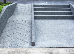 A zig-zagging wheelchair-accessible ramp runs alongside concrete steps, both bordered by green plants.