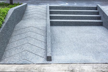 A zig-zagging wheelchair-accessible ramp runs alongside concrete steps, both bordered by green plants.