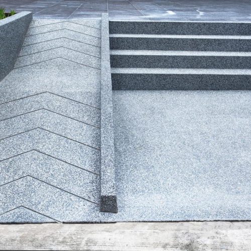A zig-zagging wheelchair-accessible ramp runs alongside concrete steps, both bordered by green plants.