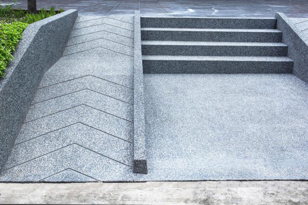 A zig-zagging wheelchair-accessible ramp runs alongside concrete steps, both bordered by green plants.