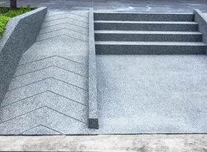Grey concrete stairs are adjacent to an accessible wheelchair ramp that features a zigzag pattern on its surface.