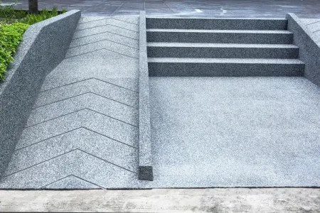 Grey concrete stairs are adjacent to an accessible wheelchair ramp that features a zigzag pattern on its surface.