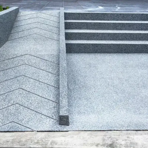 Grey concrete stairs are adjacent to an accessible wheelchair ramp that features a zigzag pattern on its surface.