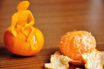 Two satsumas. The one on the right has been peeled. The one on the left has the shape of a person sitting on top of it, created from the peelings.