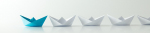 A group of white origami paper boats with one distinct blue origami paper boat standing out among them, arranged on a plain white surface.