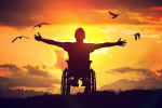 Disabled man sitting on wheelchair and stretching hands at sunset.