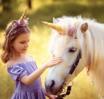 Young girl with wearing a unicorn headpiece stroking a unicorn