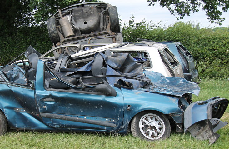 An image of a car wreck, they are others in the background Collection of Wrecked Cars in a Countryside Field.