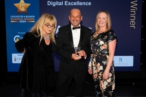 Three people pose together at the Chichester & Bognor Business Awards 2024. Clive  Loseby is in the centre, holding a trophy, is in a black tuxedo. The two women beside him are dressed formally. They stand in front of a backdrop that reads Digital Excellence Winner.