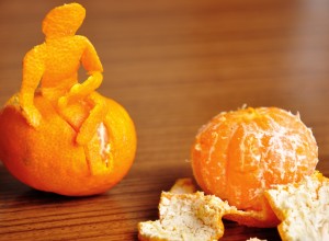 Two satsumas. The one on the right has been peeled. The one on the left has the shape of a person sitting on top of it, created from the peelings.