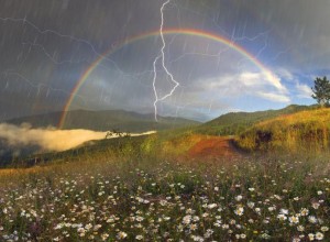 A rainbow in front of dark grey clouds, a lightning bolt is in front of it