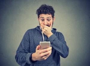 Young man looking shocked while watching breaking news on phone.