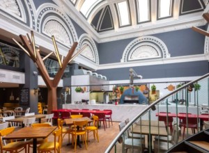 A cafe inside an old hotel. There is a curving staircase in the foreground.