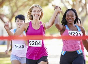 Three women runners approaching the winning tape, the two in front are holding hands in the air, looking delighted to be winning