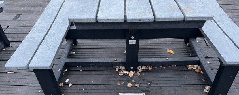 A table with 2 benches fixed to it, gaps are on the other sides for wheelchairs. A sign on the floor reads: Polite Notice Please prioritise these tables for disabled users