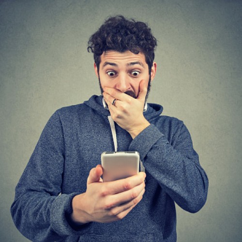 Young man looking shocked while watching breaking news on phone.