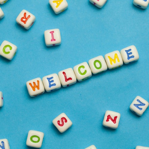 Scattered white alphabet beads with colorful letters on a blue background, with some beads arranged to spell \WELCOME\ in the center.