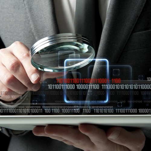 Close-up of a man in a suit holding a magnifying glass over a computer tablet with binary digits overlaid across the image