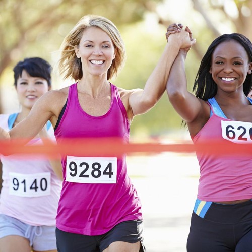 Three women runners approaching the winning tape, the two in front are holding hands in the air, looking delighted to be winning