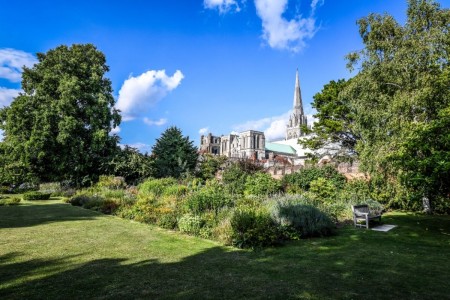 Chichester Cathedral. In the foreground is a lawn and some trees, under a blue sky