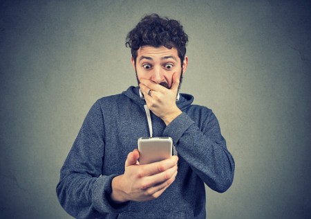 Young man looking shocked while watching breaking news on phone.