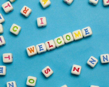 Scattered white alphabet beads with colorful letters on a blue background, with some beads arranged to spell WELCOME in the center.