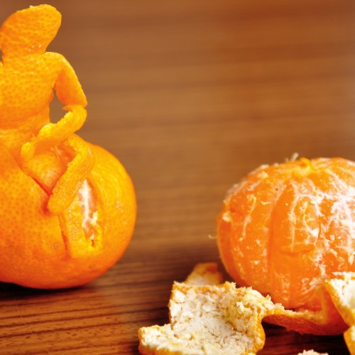 Two satsumas. The one on the right has been peeled. The one on the left has the shape of a person sitting on top of it, created from the peelings.