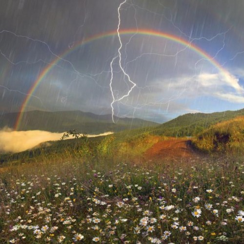 A rainbow in front of dark grey clouds, a lightning bolt is in front of it