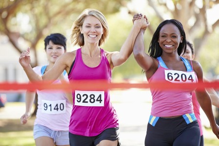 Three women runners approaching the winning tape, the two in front are holding hands in the air, looking delighted to be winning