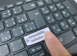 Accessibility and inclusion key on a gray keyboard. Finger pressing key 