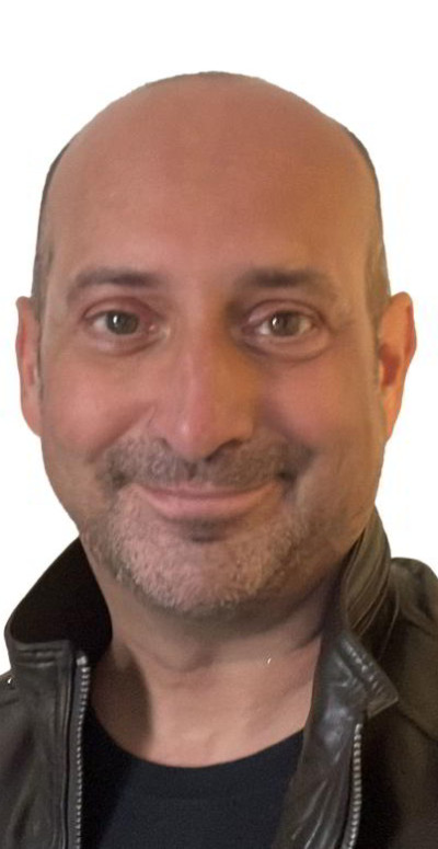 Clive has brown eyes, no hair, has shaped stubble and is smiling