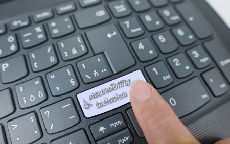 Accessibility and inclusion key on a gray keyboard. Finger pressing key