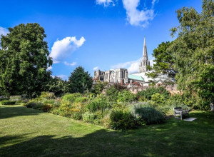 Chichester Cathedral. In the foreground is a lawn and some trees, under a blue sky