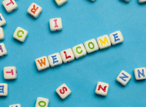 Scattered white alphabet beads with colorful letters on a blue background, with some beads arranged to spell WELCOME in the center.